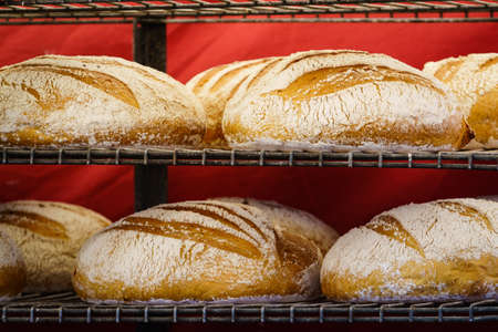 Many rustic baked traditional bread loaves on market stall outdoor.