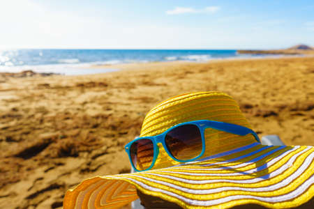 Summer and holidays, resting on seaside. Blue sunglasses and yellow straw hat on sandy beach sea shore.の写真素材