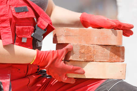 Unrecognizable woman working on construction site, building house, installing bricks. Industrial...
