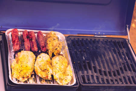Close up delicious chicken meat and sausages grilling on barbecue gas grill. Barbeque dinner...