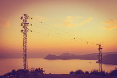 Coastline at sunset with electricity transmission pylons, power lines high voltage towers. Mesa...