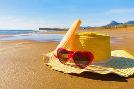 Sun protection accessories on sea shore. Red sunglasses, yellow straw hat and sunscreen cream bottle...