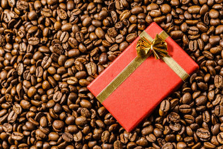 Red small gift box with bow on roasted brown coffee beans background.の写真素材