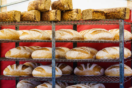Many rustic baked traditional bread loaves on market stall outdoor.