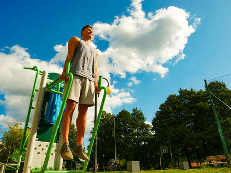 Young handsome man working out in outdoor gym. Sporty guy flexing his muscles on machine. Staying...