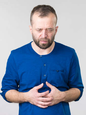 Man having huge stomach pain holding his belly feeling very unwell. Guy being sick and unhealthy.