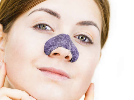 Woman appying clear-up strips on nose, using pore cleansing textile mask, on white. Girl taking care...