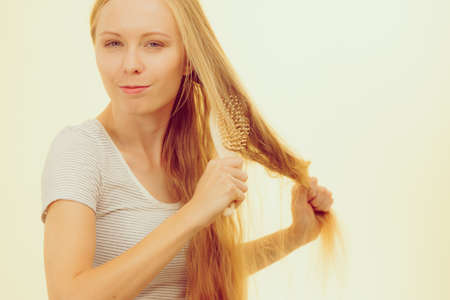 Blonde woman with brush combing her very long messy hair. Teenage girl with bad hair care.の写真素材