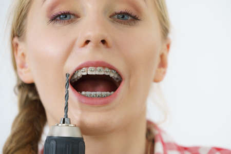 Funny teenage woman wearing teeth braces holding drill about to take brace off.