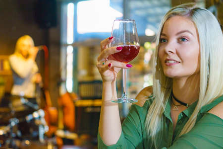 Girl with alcohol glass in club or bar at counter, female singer sing song in the backgroundの写真素材