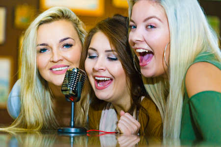 Women singing songs in karaoke club. Female friends with microphone having fun. Party, celebration, nightlife and people concept.の写真素材