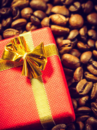 Red small gift box with bow on roasted brown coffee beans background.の写真素材
