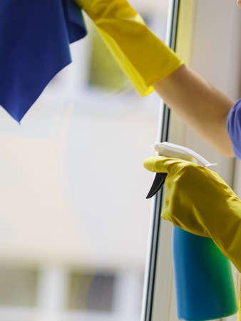 Female hand in yellow gloves cleaning window pane with rag and spray detergent. Cleaning conceptの写真素材