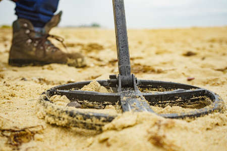 Man looking for lost objects using electronic metal detector devic on sea sandy beach. Treasure...