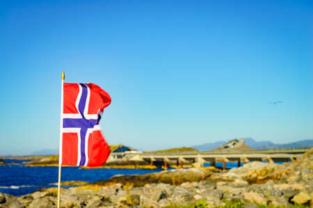 Norwegian flag against world famous Atlantic road bridge Atlanterhavsvegen in Norway Europe. National scenic route. Tourist attraction.の写真素材