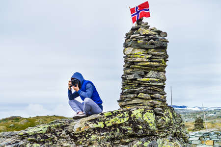 Tourist woman in mountains at high stone stack taking travel photo with camera. National tourist scenic route 55 Sognefjellet, Mefjellet viewpoint, Norwayの写真素材