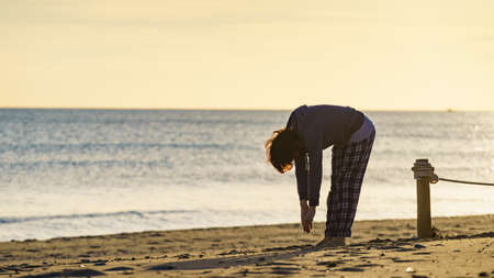 Woman in pajamas at morning time on beach. Female stretching, doing sports outdoors. Active living concept. Taking care of health. Reducing stress by exercising.の写真素材