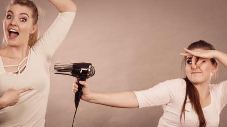 Woman drying her female friend wet armpit using hair dryer. Getting rid of sweat and bad smell, hyperhidrosis.の写真素材