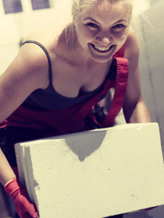 Strong pretty woman working on construction site, building house, installing gray airbricks....