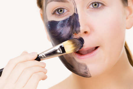 Skin care. Female applying black purifying mud mask, deep cleanser to her face, using brush. Beauty, spa and acne treatment.の写真素材
