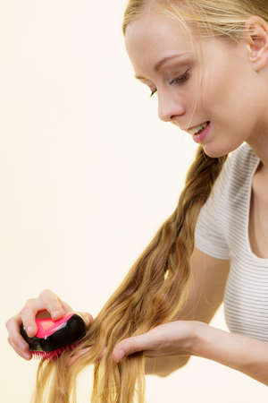 Blonde girl with long braid hair and brush. Girl taking care refreshing her hairstyle. Haircare...