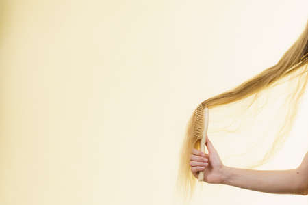 Blonde girl with brush combing her long hair. Girl taking care refreshing her hairstyle. Haircare...