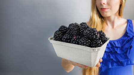 Girl holding fresh blackberry fruits in paper box. Healthy seasonal fruit, organic nutrition.の写真素材