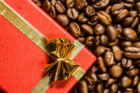 Red small gift box with bow on roasted brown coffee beans background.の写真素材