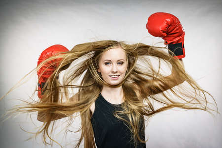 Bloned long hair girl boxer in big fun red gloves playing sports boxing. Female fight for equal rights for women.の写真素材