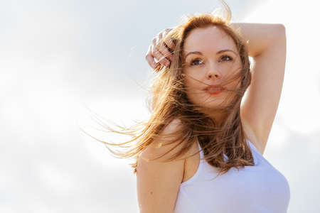 Gorgeous romantic girl outdoors. Brown long hair blowing in the wind against sky.