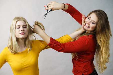 Hairstyle and haircut. Young female barber holding scissors tool ready to trimming hair her friends. Two girls creating new hairdo coiffureの写真素材