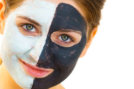 Woman with clay carbo black mask on half face and white mud on second half. Girl taking care of oily complexion. Beauty procedures. Skincare.の写真素材
