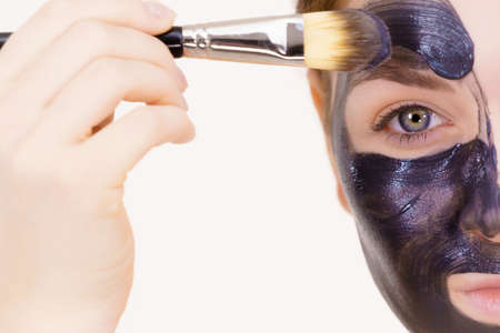 Skin care. Female applying black purifying mud mask, deep cleanser to her face, using brush. Beauty, spa and acne treatment.の写真素材