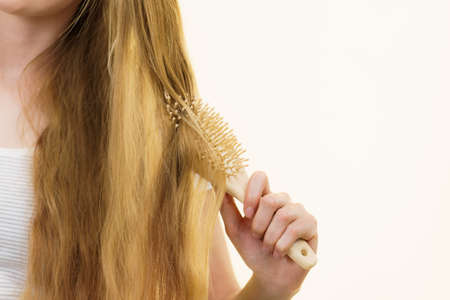 Blonde girl with brush combing her long hair. Girl taking care refreshing her hairstyle. Haircare concept.の写真素材