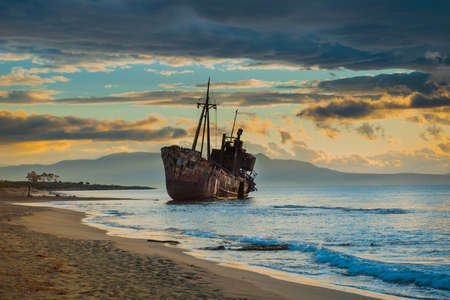 An old abandoned shipwreck, wrecked boat sunken ship stand on beach coast. Scenic sunset skyの写真素材