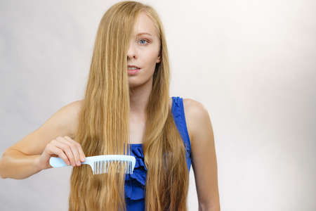 Young woman combing long healthy blonde hair, using comb