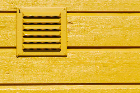 Outdoor ventilation grid in wooden yellow wall of scandinavian house