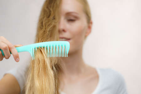 Blonde woman with comb brushing her very long messy hair. Teenage girl with bad hair care.の写真素材