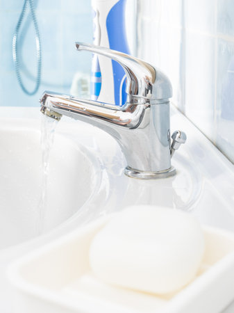 Metal bathroom clean sink tap, soap bar and oral hygiene essentials, electric toothbrush