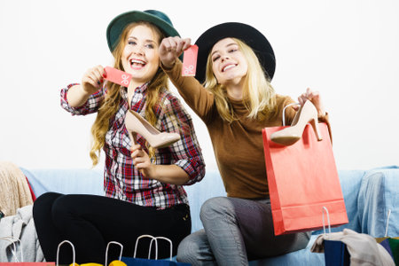 Female friends on shopping showing tag with sale percentage sign enjoying cheap clothing.の写真素材