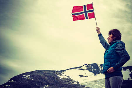 Tourist woman enjoy mountains landscape, holding norwegian flag. National tourist scenic route 55...