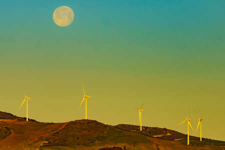 Wind turbines on hills. Full moon on sky at morning. Power generator farm for clean renewable electric energy production near Ardales, province Malaga, Andalusia Spain.の写真素材