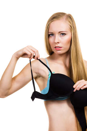 Slim blonde woman wearing underwear choosing which bra to wear, holding black push up in hand. Bosom, brassire, cup size concept.の写真素材