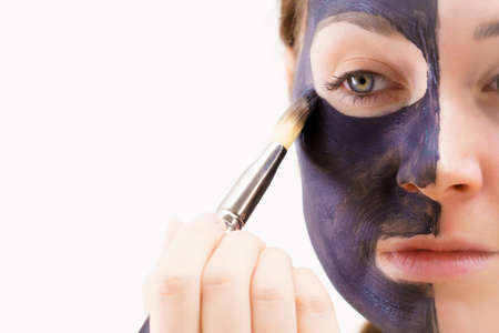 Skin care. Female applying black purifying mud mask, deep cleanser to her face, using brush. Beauty, spa and acne treatment.の写真素材