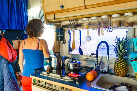 Woman inside caravan rv, looking outside from kitchen area. Cooking in campervan. Holidays,...