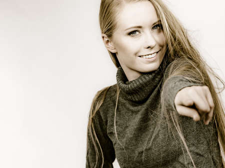 Smiling girl long blonde hair wearing warm sweater clothing pointing with finger at you.の写真素材