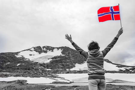 Tourist woman enjoy mountains landscape, holding norwegian flag. National tourist scenic route 55 Sognefjellet, Norwayの写真素材