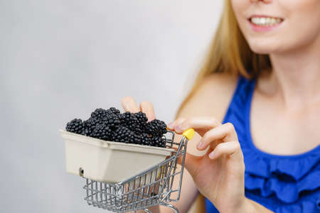 Young female holding fresh blackberry fruits box in shopping cart. Healthy seasonal fruit, organic nutrition.の写真素材