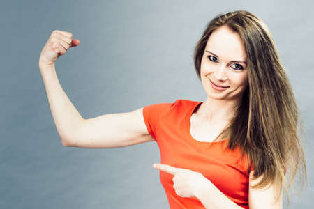 Adult woman flexing biceps and pointing with finger on her arm