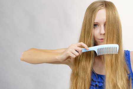 Young woman combing long healthy blonde hair, using combの写真素材